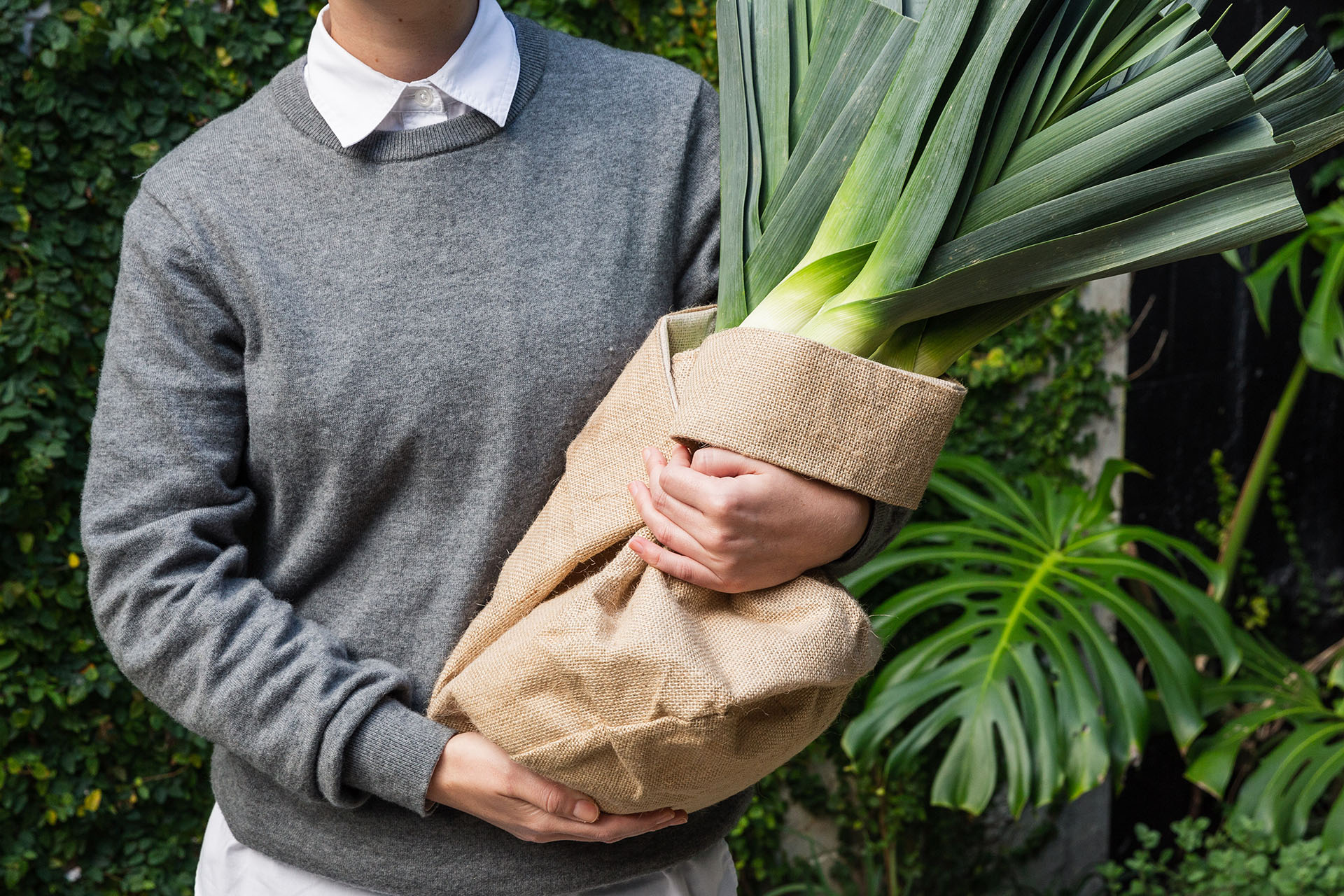 person holding a large leek in a brown sack bag